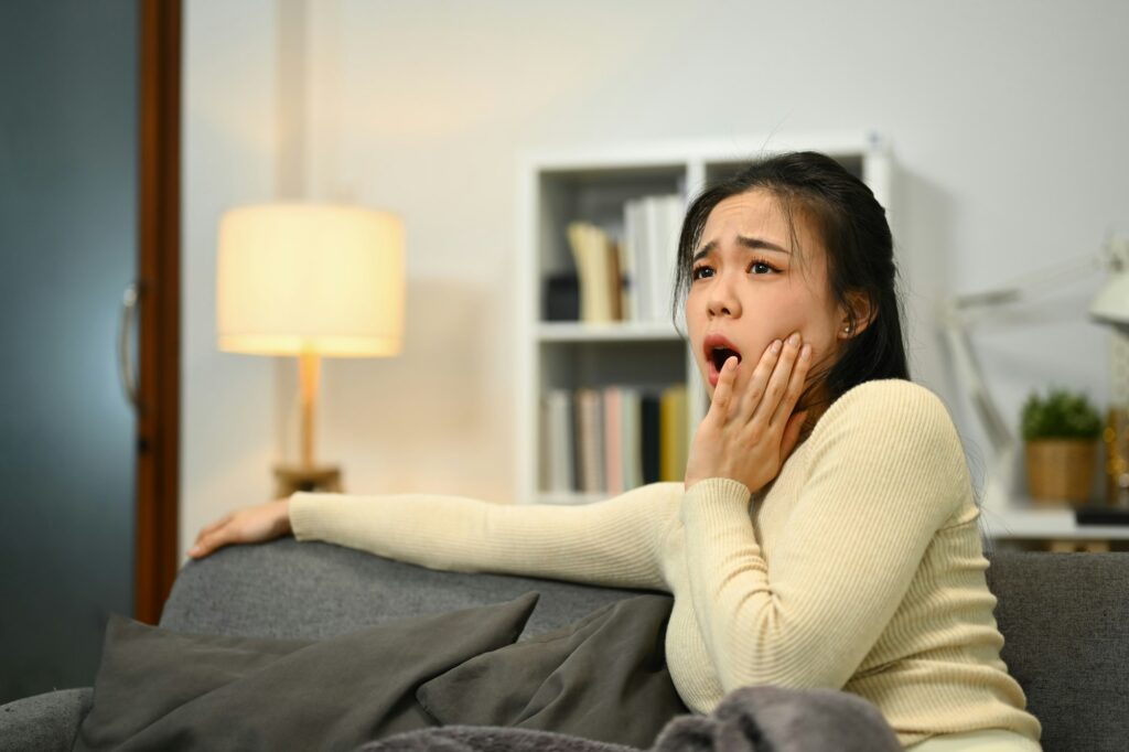 Unhappy young woman touching sore cheek suffering from toothache cavities .