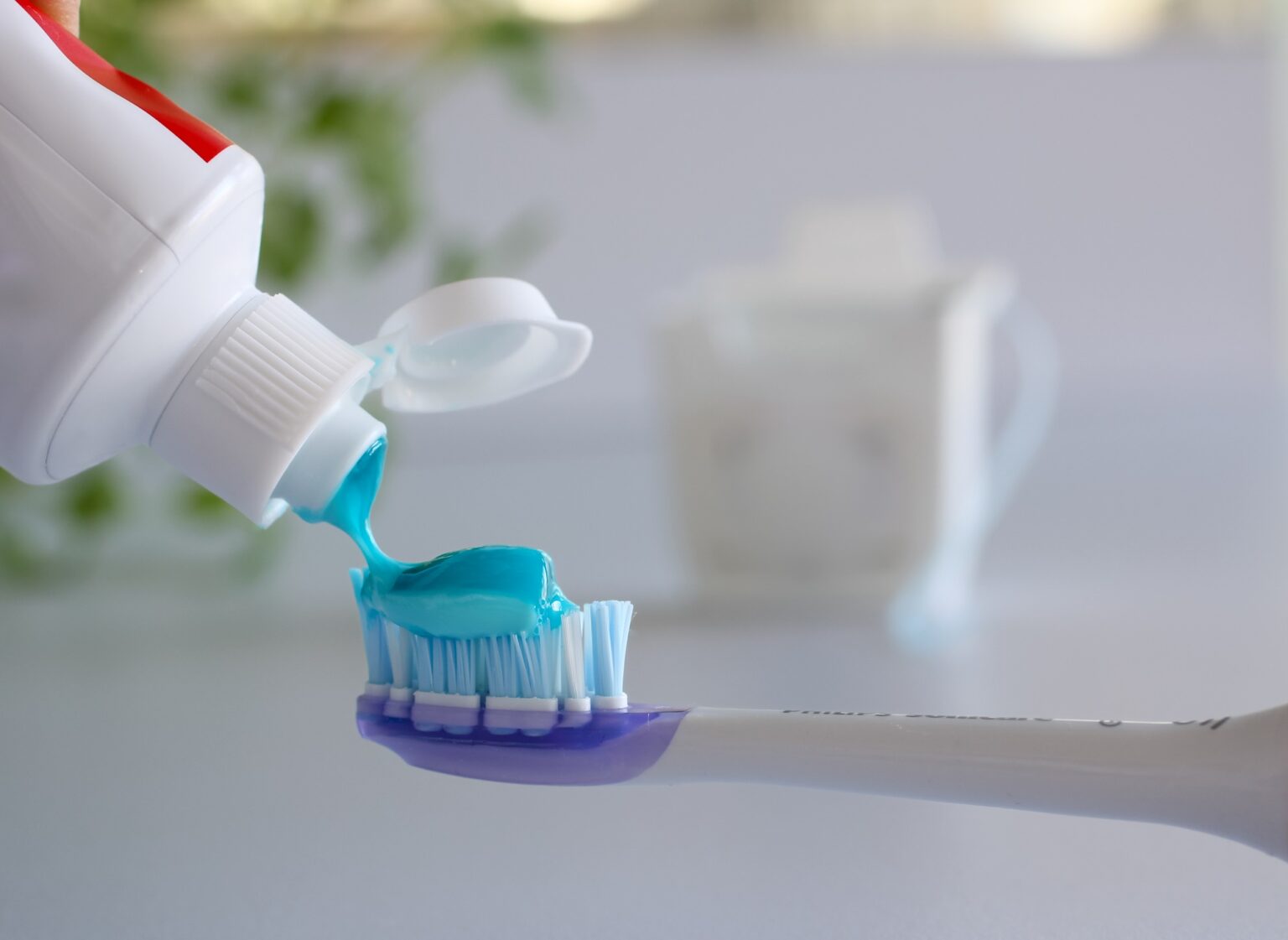 Person putting toothpaste on toothbrush with dental floss in background for dental hygiene concept