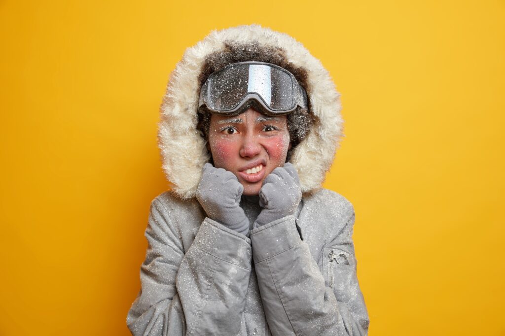 Displeased Afro American woman has face covered with ice clenches teeth from cold looks unhappily at